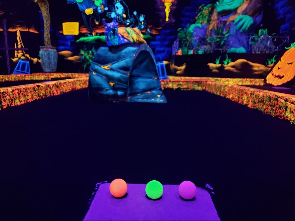 A neon orange, green and purple golf ball on a glow-in-the-dark indoor mini golf course at Monster Mini Golf.