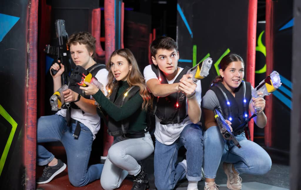 Four people having fun playing laser tag ducking behind cover in arena