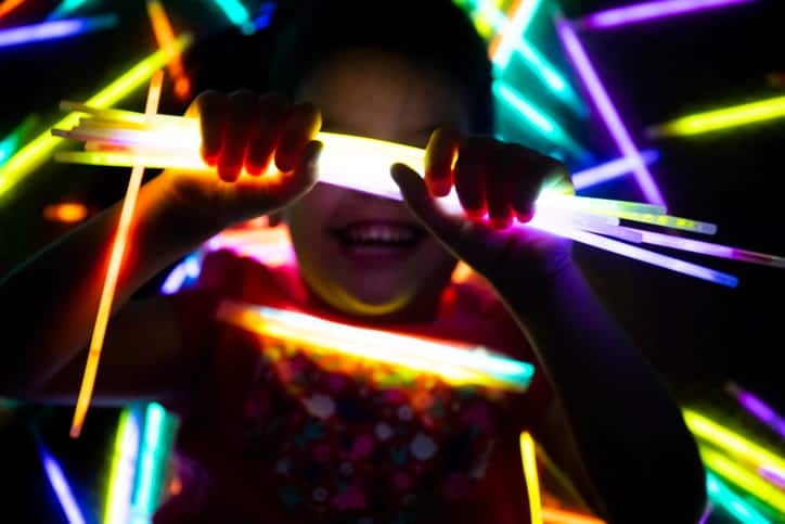 A kid smiling while surrounded by glow sticks. 